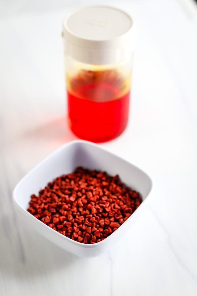 achiote oil in a jar and achiote seeds in a white bowl